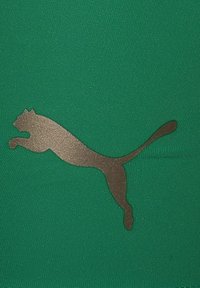 Un tissu vert au toucher lisse arbore un logo Puma métallique marron en position de saut, positionné au centre pour plus de visibilité.