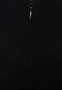 Gros plan sur une fermeture éclair en tissu noir avec une petite tirette métallique centrée verticalement dans l'image.