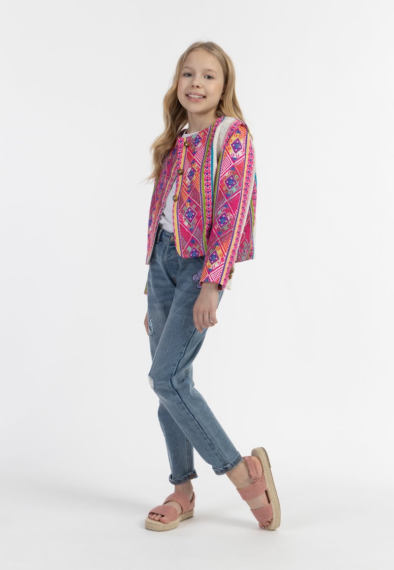 Spalvingas rožinis raštuotas švarkas su geometriniais dizainais, baltas marškinėliai, suplyšę džinsai ir rožiniai sandalai su espadrilio padu.