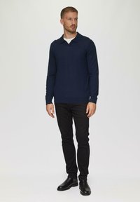 Námořnická modrá polokošile s dlouhým rukávem a plochým límečkem, spárovaná s černými slim-fit kalhotami a černými kotníkovými botami. Hladká textura.