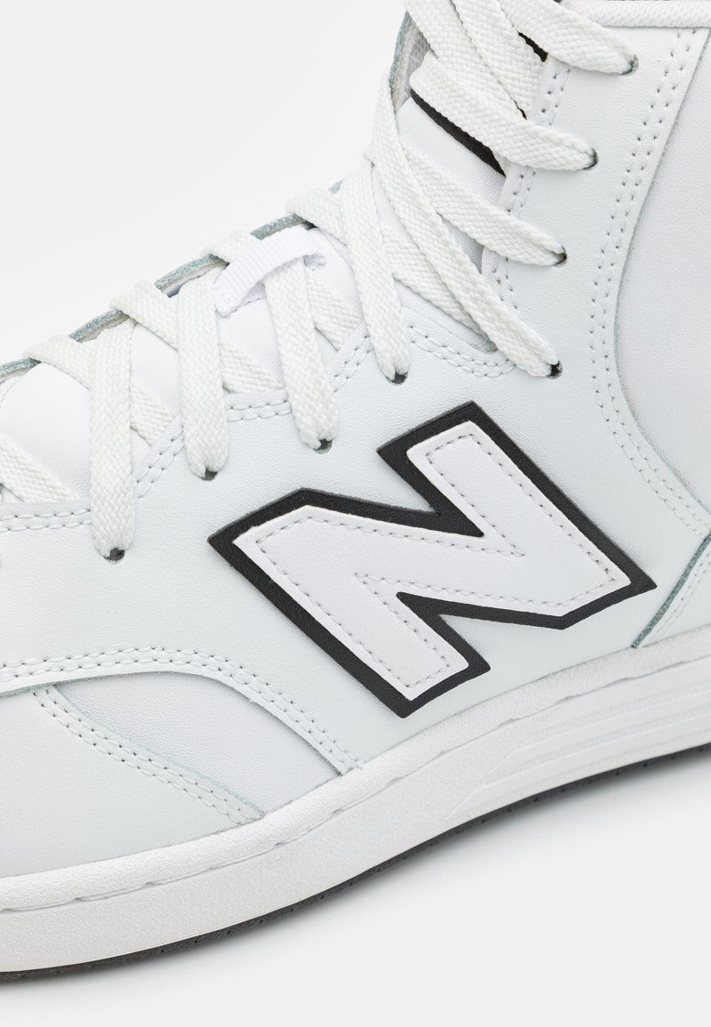 Sneaker alta bianca con tomaia in pelle, caratterizzata da dettagli neri, un grande logo "N" bianco, occhielli testurizzati e lacci bianchi piatti.