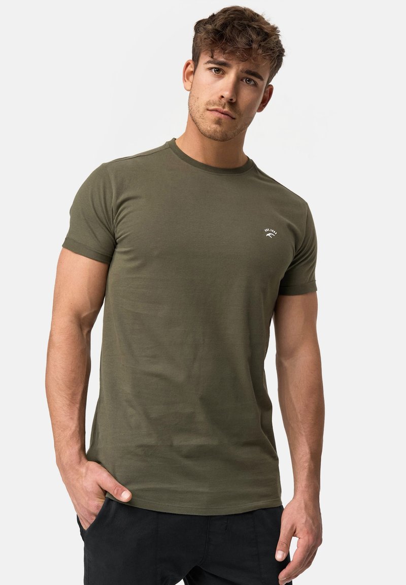 Olivgrünes kurzärmliges T-Shirt aus weichem Baumwollstoff mit rundem Halsausschnitt und kleinem Logo auf der Brust. Glatte Textur, figurbetontes Design.