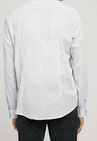 Biała koszula z długim rękawem w cienkie granatowe paski, o prostym kroju, z zapinanymi mankietami i lekko zaokrąglonym dołem.