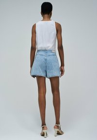 Pantalones cortos de mezclilla de color azul claro con un diseño de cintura alta, que presentan un corte recto, costuras visibles y una etiqueta en la cinturilla trasera.