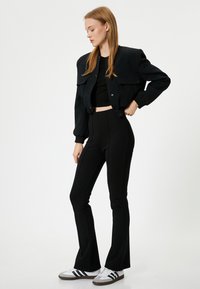 Veste bomber noire cropped avec deux poches avant, associée à un pantalon noir taille haute avec des coutures latérales et des baskets blanches avec des rayures noires.