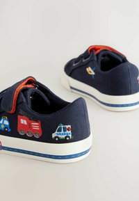 Marinblå kanvas sneakers med broderade fordonsteckningar, inklusive en brandbil och en polisbil. Vit sula med blå accentrand.