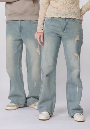 Two people wearing light blue distressed jeans and casual sneakers, standing side by side against a plain background.