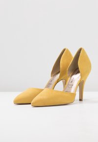 Scarpe con tacco alto in suede giallo, con punta affilata e lati sagomati. Caratterizzate da un sottile tacco a spillo e da una fodera interna liscia.