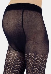 Le calze nere a motivo presentano una vita a costine e intricate decorazioni a rombo lungo le gambe. Il materiale appare semi-trasparente con una finitura testurizzata.