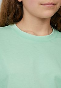 Minzgrünes Baumwoll-T-Shirt mit klassischem Rundhalsausschnitt und weicher Textur, das glattes Material und minimale Nähte zeigt.