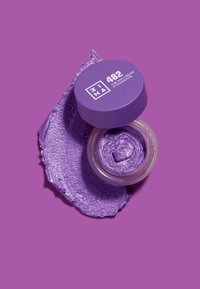 Lilla kremøyenskygge i en klar krukke, med matchende lokk og etikett. Jevn tekstur med en glitrende finish, delvis påført på en overflate.