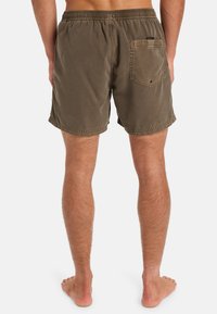 Hnědé plavkové šortky s elastickým pasem, vybavené zadní kapsou a šitými okraji. Textura vypadá hladce, vhodné pro vodní aktivity.