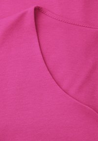 Primer plano de tela rosa continua con un borde doblado y detalle de costura suave en un diseño curvo.