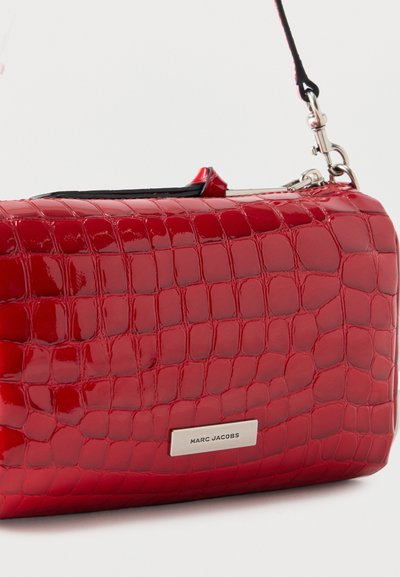 Κόκκινη γυαλιστερή τσάντα με μοτίβο κροκόδειλου, ασημένια πλακέτα με το λογότυπο Marc Jacobs και μαύρο λουράκι προσαρτημένο σε ασημένιο μεταλλικό κούμπωμα.