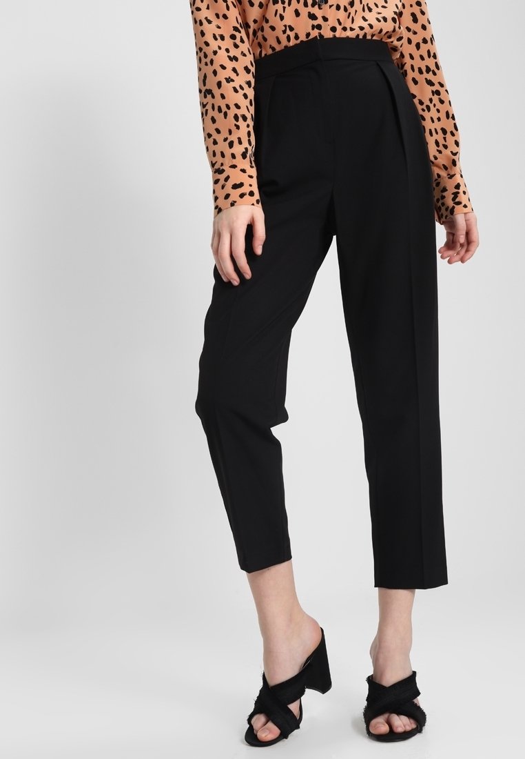 Svarta skräddarsydda byxor med hög midja, veckad front och avsmalnande ben. Matchas med en beige leopardmönstrad blus och svarta klacksandaler.