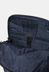 Interno di una borsa in nylon nera con una texture liscia, diversi scomparti e un motivo a logo su tutta la superficie. Chiusura con zip nella parte superiore.