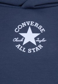 Mörkblå bomullshoodie med vit cirkulär logotyp som visar en stjärna och texten: "CONVERSE," "Chuck Taylor," och "ALL STAR." Enkel, ren design.