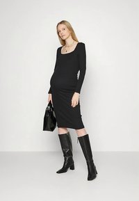 Vestido preto justo de manga comprida com decote quadrado, comprimento até ao joelho, combinado com botas pretas até ao joelho e uma mala preta.