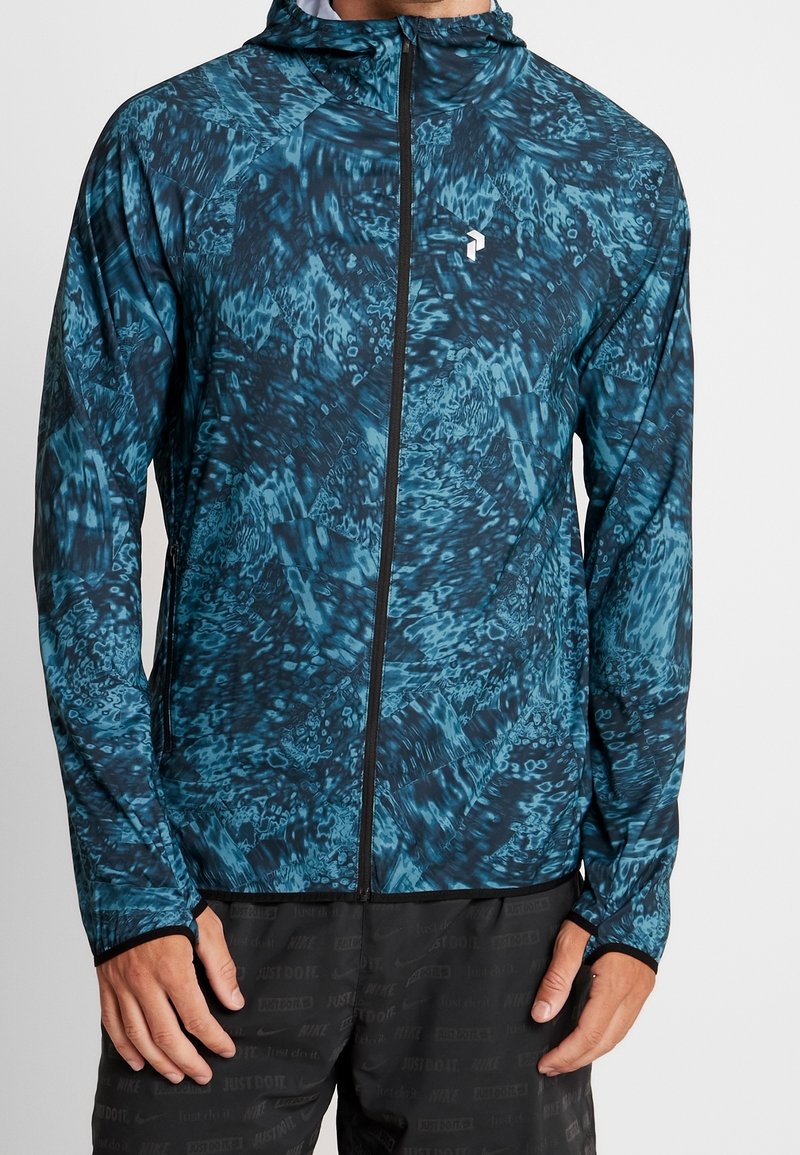 Veste légère à capuche avec un motif abstrait bleu et noir, dotée d'une fermeture éclair intégrale et d'ouvertures pour les pouces aux poignets pour un maintien sécuritaire.