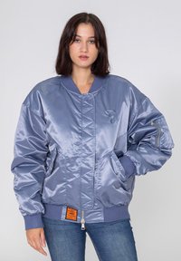 Jasnoniebieska satynowa kurtka bomberka z kwiltowanym wzorem, ściągaczami w mankietach, bocznymi kieszeniami oraz pomarańczową metką na dolnym brzegu.