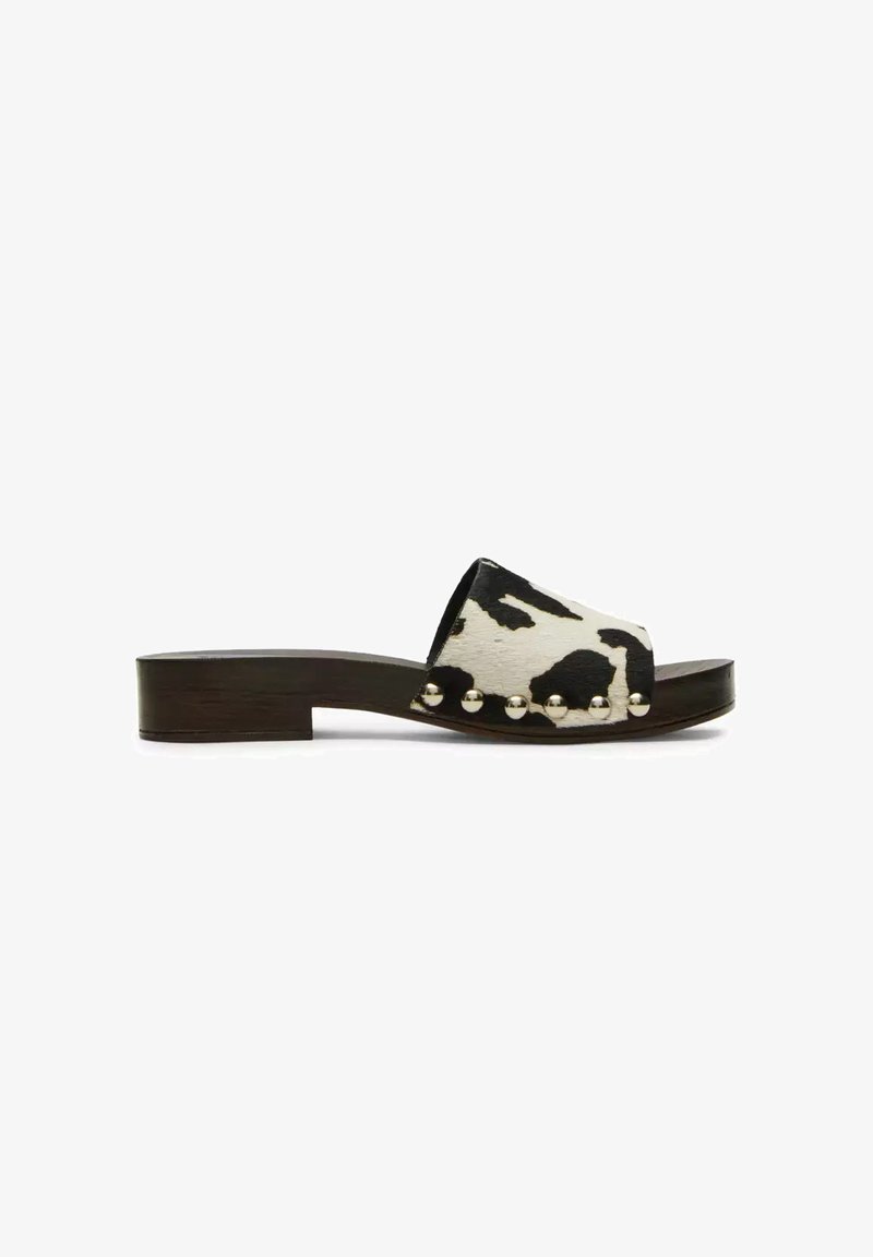 Sandale à talon bas avec semelle en bois foncé, bride imprimé vache noir et blanc, et détails de clous ronds en argent sur les côtés.