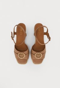 Sandales à plateforme en cuir tan avec une large sangle, une boucle géométrique dorée décorative et une sangle à la cheville. Semelle texturée de style jute.
