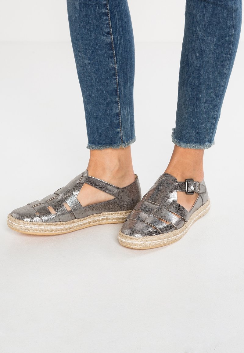 Des sandales espadrilles gris métallisé présentent un design tissé avec des découpes, une sangle avec une boucle et une semelle en jute.