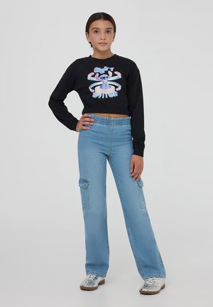 Maglietta nera a maniche lunghe e taglio cropped con design grafico, abbinata a jeans cargo azzurri chiari con tasche frontali e cintura elastica.