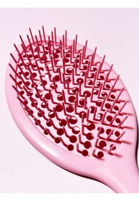 Brosse à cheveux rose en forme ovale avec des poils flexibles, des trous ronds et un manche lisse. Le design permet un démêlage facile.