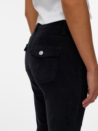 Pantalon en velours côtelé noir avec un tissu texturé, doté de poches arrière et d'un détail de bouton en métal. Design slim fit, présenté de profil.