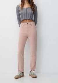 Jeans rose clair à coupe droite, fermeture à boutons sur le devant et deux poches latérales. Associés à un haut gris crop top à manches longues et des baskets.