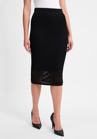 Schwarzer Strick-Bleistiftrock mit strukturiertem Muster und geripptem Bund. Mit einer Länge unterhalb des Knies und durchbrochenen Details am Saum.