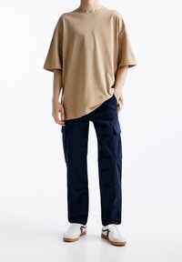 Beige katoenen T-shirt met een ontspannen pasvorm en korte mouwen, gecombineerd met donkerblauwe cargobroek met zijzakken en een rechte pijp. Witte sneakers.