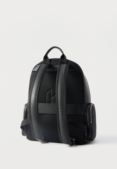 Sac à dos noir en cuir et mesh vu de dos avec bretelles rembourrées, une poignée supérieure et des poches latérales zippées.
