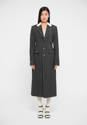 Long manteau gris charbon avec des détails de couture blanche, col à cran, deux poches avant et une fermeture à un bouton.