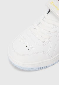 Hvid sneaker med en glat læderoverdel, perforeret tåboks, hvide snørebånd og en gennemsigtig lys blå gummisål. Har en velcro-rem.