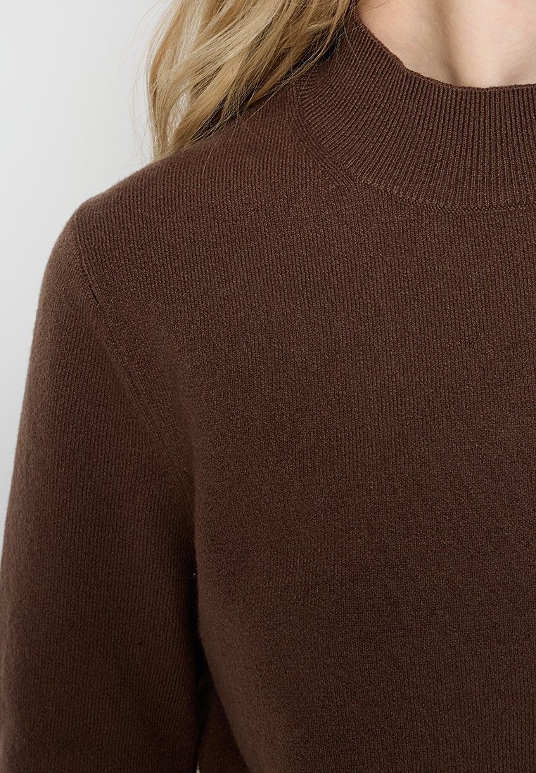 Brauner Strickpullover mit hohem, geripptem Kragen und weicher Textur. Der Stoff wirkt leicht und hat eine glatte Oberfläche.