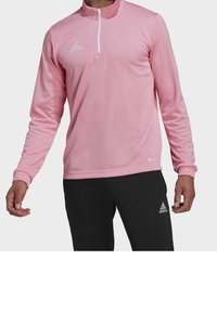 Ljusrosa långärmad tröja med halvmångdragkrage, elastiska ärmslut och vit Adidas-logotyp på bröstet, tillsammans med svarta byxor.