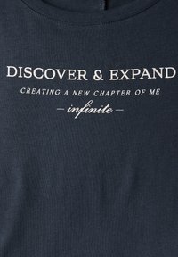T-shirt bleu marine foncé en coton doux, avec un texte blanc : "DÉCOUVRIR & ÉLARGIR CRÉER UN NOUVEAU CHAPITRE DE MOI infini" en plusieurs tailles de police.