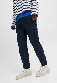 Marineblaue Cargohosen mit Seitentaschen, elastischen Bündchen und glatter Textur. Kombiniert mit einem gestreiften Stricktop und hellen Sneakern.