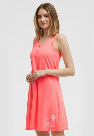 Frau mit schulterlangem Haar trägt ein ärmelloses korallenfarbenes Kleid mit Knöpfen und "Souix the Beach" Text sowie Palme-Grafik am Saum.