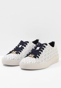 Baskets en toile avec un motif blanc et des accents du logo "MK", lacets bleu marine et semelle en caoutchouc crème. Design plat et profil bas.