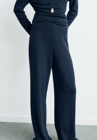 Pantaloni largi bleumarin dintr-un material moale și neted, cu o croială ajustată; talie înaltă și detalii minimale.