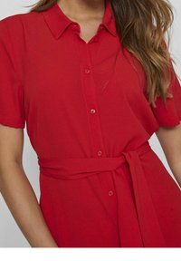 Robe courte à manches courtes rouge avec un devant boutonné et une ceinture nouée à la taille. Confectionnée dans un tissu léger à la texture lisse.