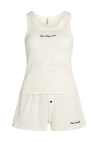 Kerman neulepuku setti vaaleassa cream-sävyssä, jossa on tanktoppi leveillä olkaimilla ja shortsimaiset housut napitti yksityiskohdalla ja logopistolla.