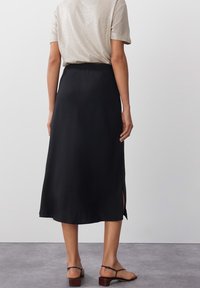 Mustat midi-hameet, joissa on sileä pinta ja joustava vyötärö, sivuhalkiot ja ilmava muotoilu. Yhdistetty vaalean metallinhohtoiseen toppiin.