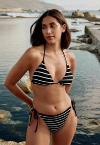 Bikini a righe bianche e nere con top triangolare e slip laterali regolabili con laccetti. Texture a coste, design minimalista e spalline sottili.
