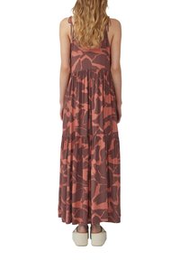 Maxikleid mit dünnen Trägern, das ein braunes und korallenfarbenes abstraktes Muster, ein gestaffeltes Design und eine entspannte Passform aufweist. Weicher Stoff und neutrale Fußbekleidung.
