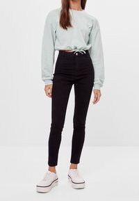 Svarta högmidjade jeans i kombination med en mintgrön kortärmad sweatshirt med dragsko och långa ärmar. Vita plattformssneakers fulländar looken.