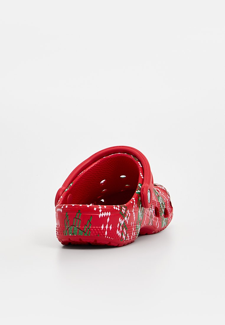 Zoccoli di plastica rossi con cinturino posteriore, caratterizzati da una superficie texturizzata con un motivo di diamanti verdi e bianchi. Voragini aperte per ventilazione.